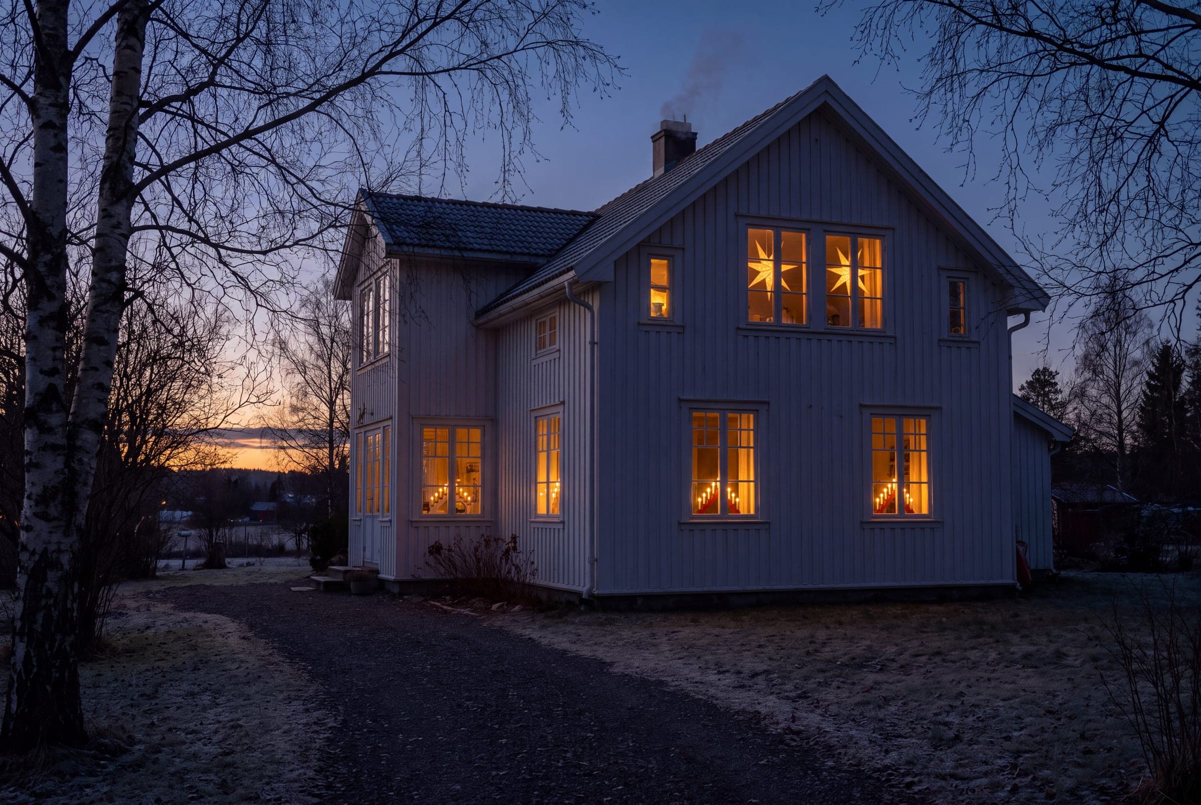 Hus i desemberskumring med blanke vinduer og adventsstjerner